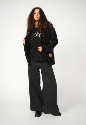 Cardigan negru din tricot cu model în cablu, asociat cu un maiou negru cu litere albe. Blugi negri, largi și cizme groase negre.