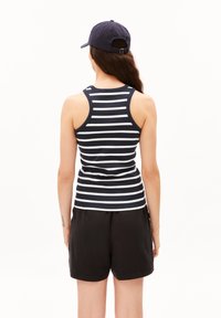 Top a righe blu e bianche con un design aderente, abbinato a pantaloni corti neri. La persona indossa un cappellino da baseball scuro, vista da dietro.