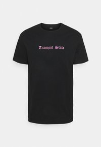 Svart bomullströja med korta ärmar som pryds av texten "Tranquil State" i rosa stiliserad font över bröstet. Normal passform.