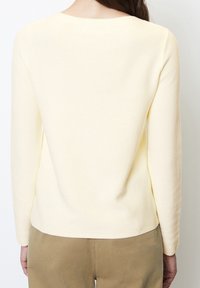 Pull jaune clair à manches longues avec un design en maille texturée, encolure arrondie et ourlet droit, associé à un pantalon beige.