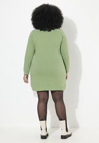 Robe-sweat en coton vert avec des manches longues, des poignets côtelés et une coupe droite. Portée par-dessus des collants noirs et des bottines crème.