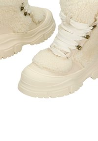 Robuuste, crèmekleurige laarzen met een getextureerde shearling bovenkant, witte veters en metalen oogjes. Dikke rubberen zool met groeven voor grip.