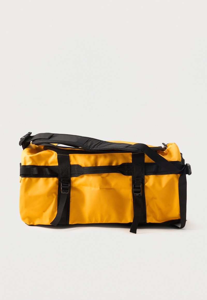 Gelbe und schwarze Reisetasche mit mehreren Riemen und Schnallen, gefaltet und auf weißem Hintergrund liegend dargestellt.