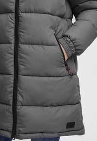 Gray puffer jacket with horizontal quilted design, front zipper, elastic cuffs, and side pockets. Fabric appears smooth and water-resistant.