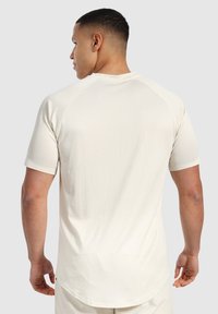 Camisa atlética de manga corta color beige claro con una tela texturizada y mangas raglán. Presenta un dobladillo redondeado y detalles de costura sutiles.