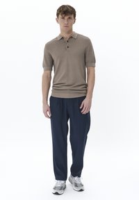 Camiseta de polo beige de manga corta con un patrón texturizado, tres botones y un cuello, combinada con pantalones holgados azul marino y zapatillas grises.