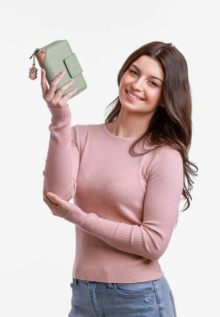 Green zippered wallet with a textured finish and a decorative charm held by a woman in a pink ribbed sweater.