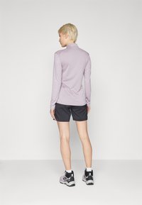 Top de mangas longas lilás claro combinado com calções pretos e sapatilhas de desporto cinzas. Design simples, textura suave e ajuste funcional.