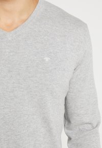 Maglione grigio a V in tessuto tricot morbido; presenta un logo discreto sul petto e maniche lunghe con una fine lavorazione.
