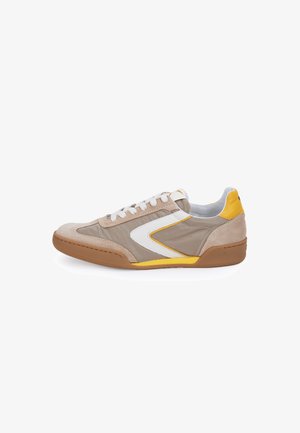 Zapatilla de perfil bajo con ante beige, paneles de tela en taupe, detalles en blanco y amarillo, cordones blancos y suela de goma marrón, vista desde el lateral exterior.