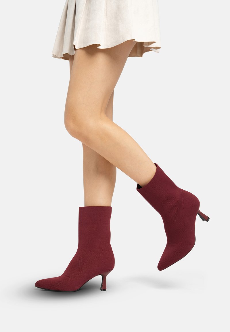 Bottes chaussettes bordeaux à la cheville avec un bout pointu et un petit talon fin. Matière textile lisse avec un design ajusté, sans éléments métalliques visibles ni motifs.