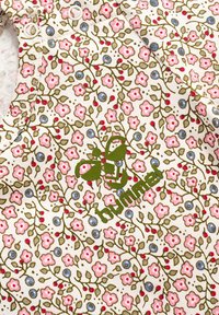 Witte stof met een bloemenpatroon van roze bloemen, blauwe cirkels en groene bladeren; bevat een groen logo met een bijmotief.