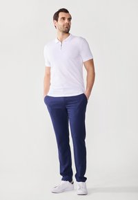 Hvit kortermet polo skjorte med glidelås ved halsen, kombinert med mørk marineblå slim-fit bukser og hvite sneakers, som viser et rent design.