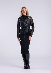 Veste de motard en cuir noir avec une taille ceinturée, des manches longues transparentes et un devant zippé, superposée à une robe noire ajustée et des bottes à genoux.