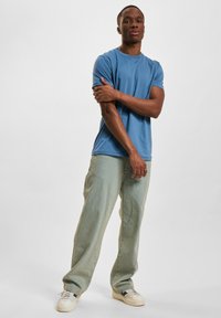 Lys blå bomull T-skjorte, rund hals, tettsittende ved skuldrene. Kombinert med lysegrønne vide jeans, brukt med beige sneakers.