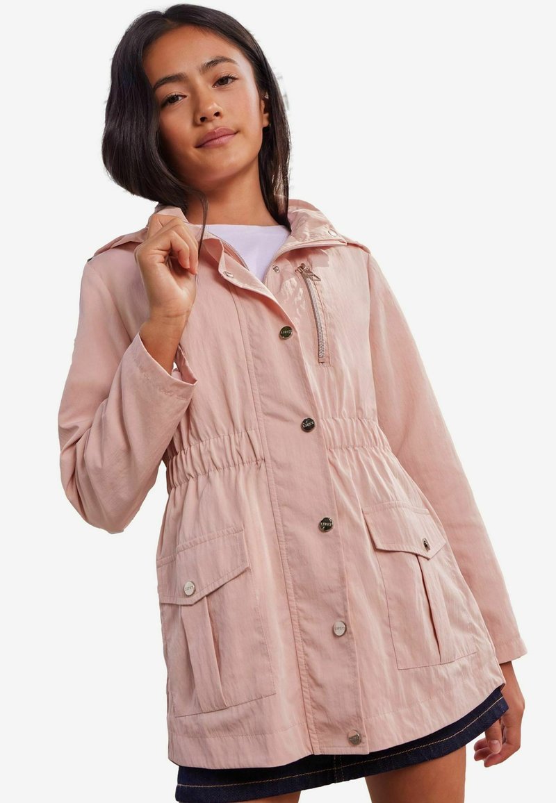 Chaqueta rosa claro con cintura ajustable, capucha regulable, dos bolsillos frontales y detalles en hardware plateado. Textura de tela suave.