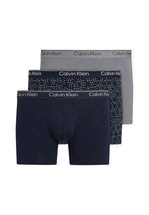 Tre paia di boxer da uomo Calvin Klein in grigio tinta unita, blu navy con puntini astratti grigi e blu navy tinta unita, impilati uno davanti all'altro.