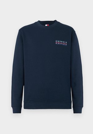 Temno modra majica s crewneck izrezom in dolgimi rokavi, z ribanim zaključkom na rokavih in kroju, na levi strani prsi pa se nahaja majhen logotip "1985 Tommy Jeans".