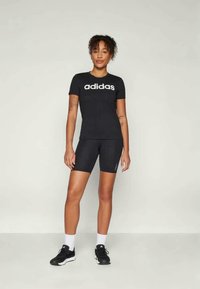 Black short-sleeve T-shirt with white "adidas" logo, paired with black bike shorts. Black athletic shoes and white socks complete the look.
