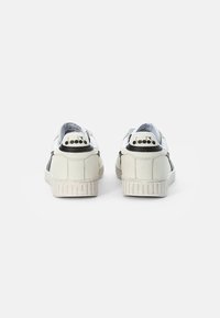 White leather sneakers with black accents, a textured rubber sole, and a logo on the heel. The design features a low-top silhouette.