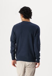 Ναυτικό μπλε φούτερ με μακριά μανίκια και στρογγυλή λαιμόκοψη, κατασκευασμένο από μαλακό βαμβακερό ύφασμα, με χαλαρή εφαρμογή και ριμπ τελείωμα.