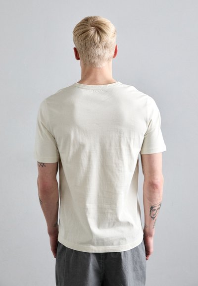 Tricou din bumbac bej deschis, cu mânecă scurtă și decolteu rotund. Textură netedă, design simplu și fără grafice vizibile.