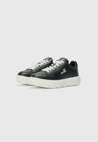 Zwarte leren sneakers met witte rubberen zolen, voorzien van geperforeerde details, contrasterende veters en een logo aan de zijkant gedrukt.