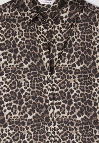 Beżowo-czarna bluzka w cętki z klasycznym kołnierzykiem, zapięciem na guziki i gładką fakturą materiału. Rozmiar: S.