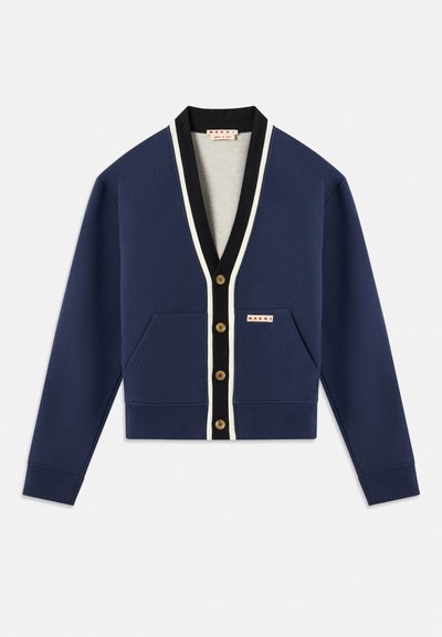 Námořnický svetr s bílými a černými akcenty, s výstřihem do V, zapínáním na knoflíky a dvěma předními kapsami. Texturovaná tkanina a zlaté knoflíky.