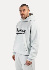 Felpa leggera grigia con testo in corsivo nero "Smidbx" sulla parte anteriore, dotata di tasca a kangaroo, polsini a coste e cappuccio con coulisse.