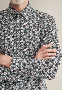 Blumenhemd mit braunem Grund und weißen sowie türkisfarbenen Blumen. Hergestellt aus leichtem Stoff, hat es einen klassischen Kragen und eine Knopfleiste.
