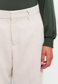 Pantalon en velours côtelé beige avec des rayures verticales, doté de poches latérales et d'un devant plat. Assorti à un haut vert avec des manches froncées.