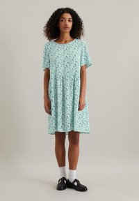 Lichtblauwe jurk met korte mouwen, gathered taille en een verspreid bloemenprint. Draag met witte sokken en zwarte instappers.