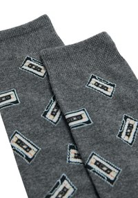 Calcetines grises hechos de tela suave presentan patrones repetidos de cintas de casete en negro, azul y naranja, con puños acanalados en la parte superior.