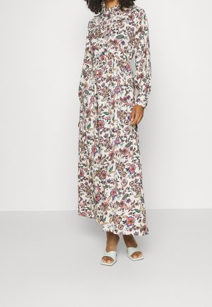 Robe maxi à manches longues en tissu léger, dotée d'un motif floral coloré sur fond blanc, avec un col haut et une silhouette fluide.