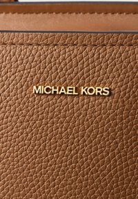 Brązowy skórzany portfel o teksturowanej powierzchni z złotym logo "MICHAEL KORS", charakteryzujący się strukturą przypominającą kamyczki oraz prostym wzornictwem.