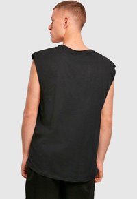 Svart ermeløs t-skjorte med rund hals, avslappet passform og lett senket skuldersømmer. Stoffet ser glatt ut med en uformell drapering.