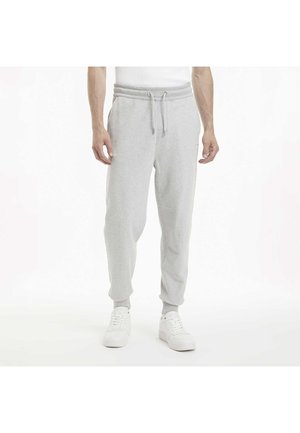 Pantalones de chándal gris claro con una cinturilla adjustable, piernas entalladas y bolsillos laterales, hechos de una tela suave y texturizada. Combinados con zapatillas blancas.