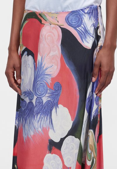 Gros plan d'une personne portant une jupe avec un motif abstrait coloré en rouge, bleu, rose, blanc et noir.