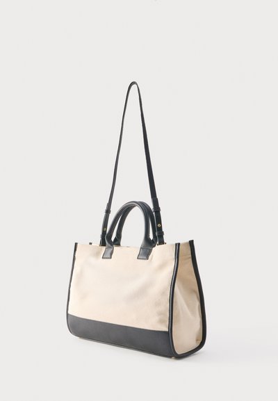Μπεζ τσάντα tote από καμβά με μαύρες δερμάτινες λεπτομέρειες, διπλές κοντές λαβές και ρυθμιζόμενο μακρύ ιμάντα ώμου.