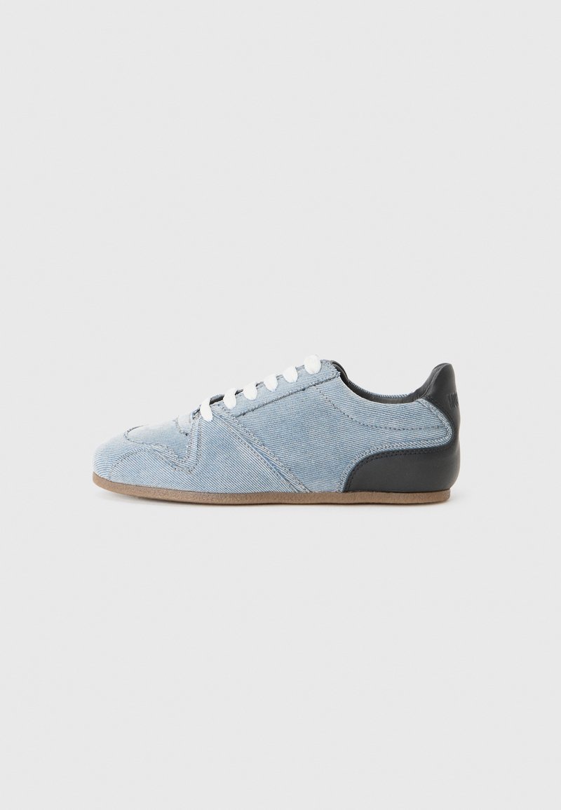 Denim sneaker with light blue canvas upper, black leather heel, white laces, and rubber sole. Features seam detailing and a rounded toe.