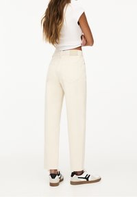 Pantalon taille haute de couleur crème avec une coupe droite, doté de poches arrière et d'une passants de ceinture. Associé à des baskets avec des accents noirs.