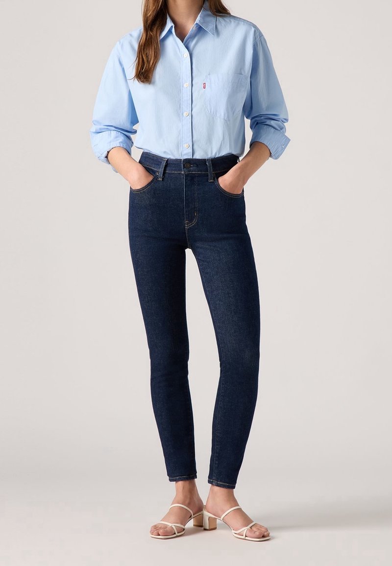 Chemise boutonnée bleu clair avec une poche poitrine, associée à un jean skinny noir et des sandales blanches à lanières avec un talon carré.