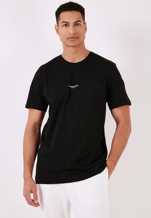 Tricou negru din bumbac, cu mâneci scurte, decolteu rotund și un detaliu central cu logo alb. Croiala este lejeră, iar textura este netedă.