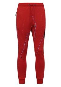 Rode joggingbroek met een koord in de tailleband, voorzien van blauw en zwart verfspatontwerpen en een ritszak aan de zijkant. Aansluitende enkels.