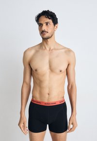 Black boxer briefs with a red waistband labeled "BJÖRN BORG." The fabric appears smooth, and the design is form-fitting with no visible patterns.