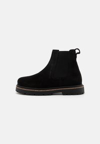 Botine Chelsea din velur negru, cu panouri elastice pe laterale, tab pentru tragere și talpă din cauciuc texturat. Prezintă un profil jos și o talpă medie de nuanță cafenie în contrast.