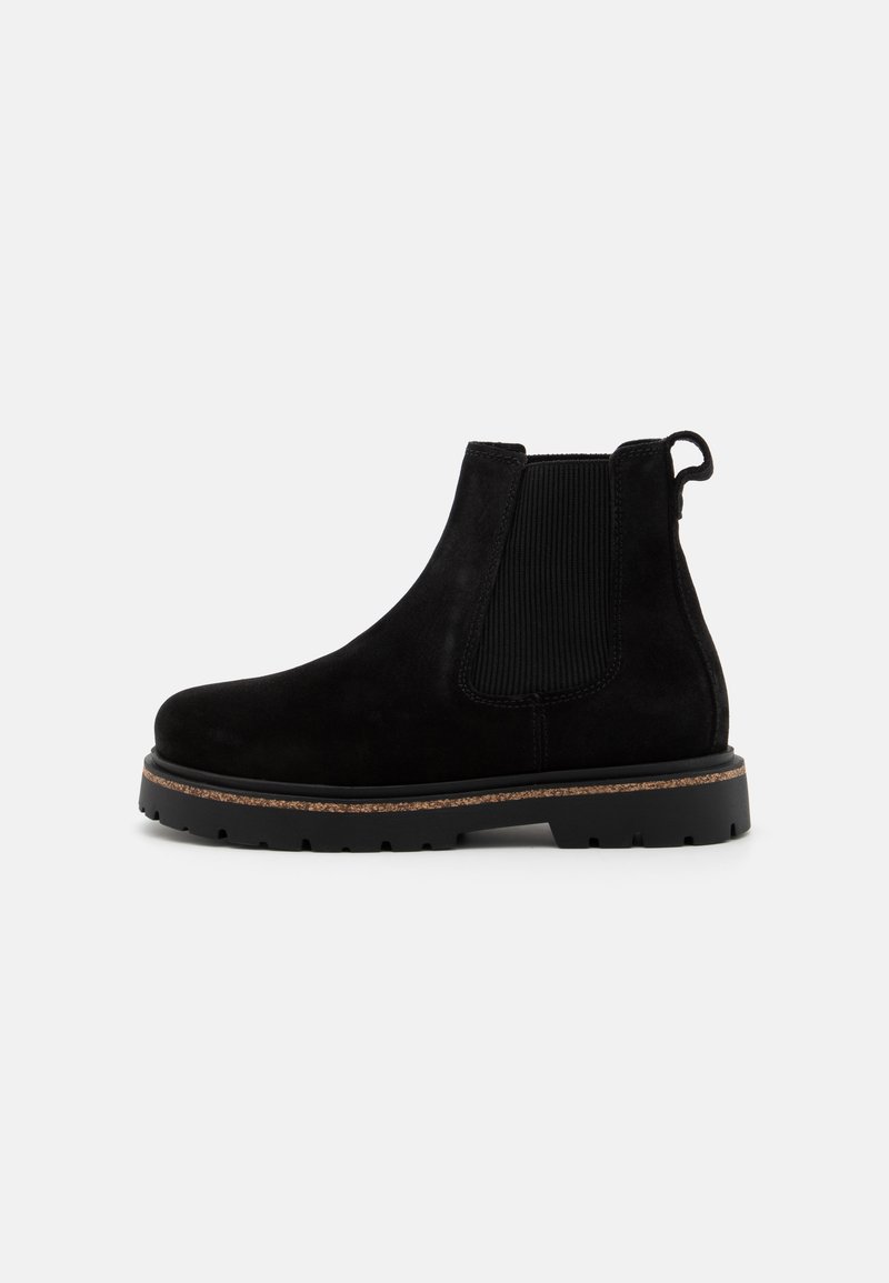Botine Chelsea din velur negru, cu panouri elastice pe laterale, tab pentru tragere și talpă din cauciuc texturat. Prezintă un profil jos și o talpă medie de nuanță cafenie în contrast.