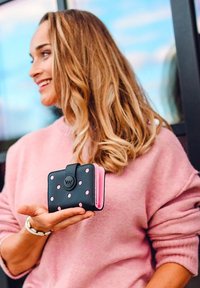 Black wallet with pink polka dots, folded design, and a circular clasp. The interior features pink accents and card slots.