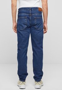 Vaqueros de mezclilla en azul oscuro con un diseño de pierna recta. Cuenta con dos bolsillos traseros y una etiqueta de cuero marrón en la cinturilla.